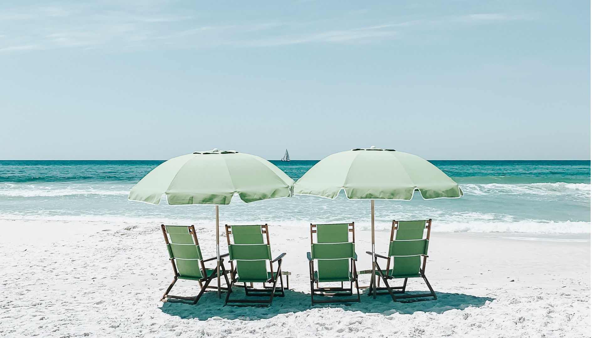Four green beach chairs and umbrellas facing the ocean